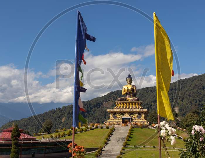 Buddha statue with clouds in the background and prayer flags in the foreground