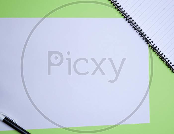 Creative Flay Lay, Table Top For Students, Office, Business Work. Spiral Notebook, Black Pen, White Sheet On A Green Background