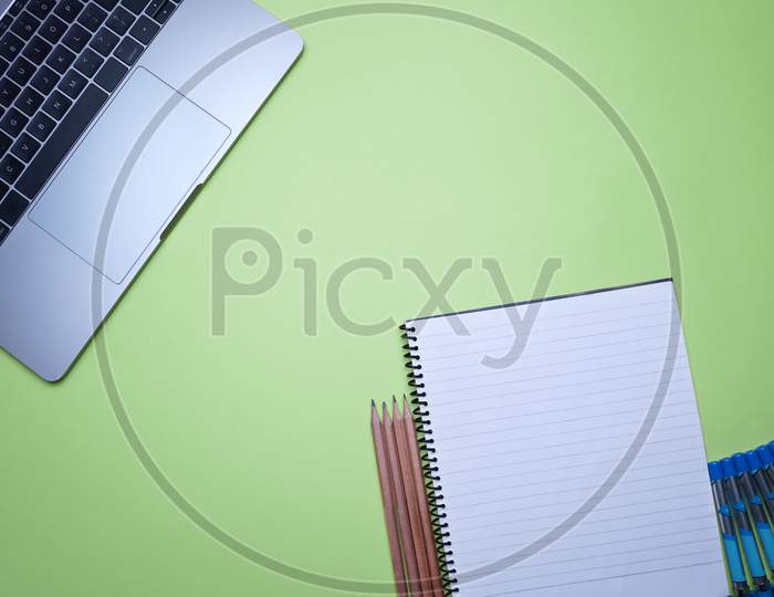 Table Top Flat Lay Of Office. Top View Laptop, Spiral Notebook And Pencils On A Green Background