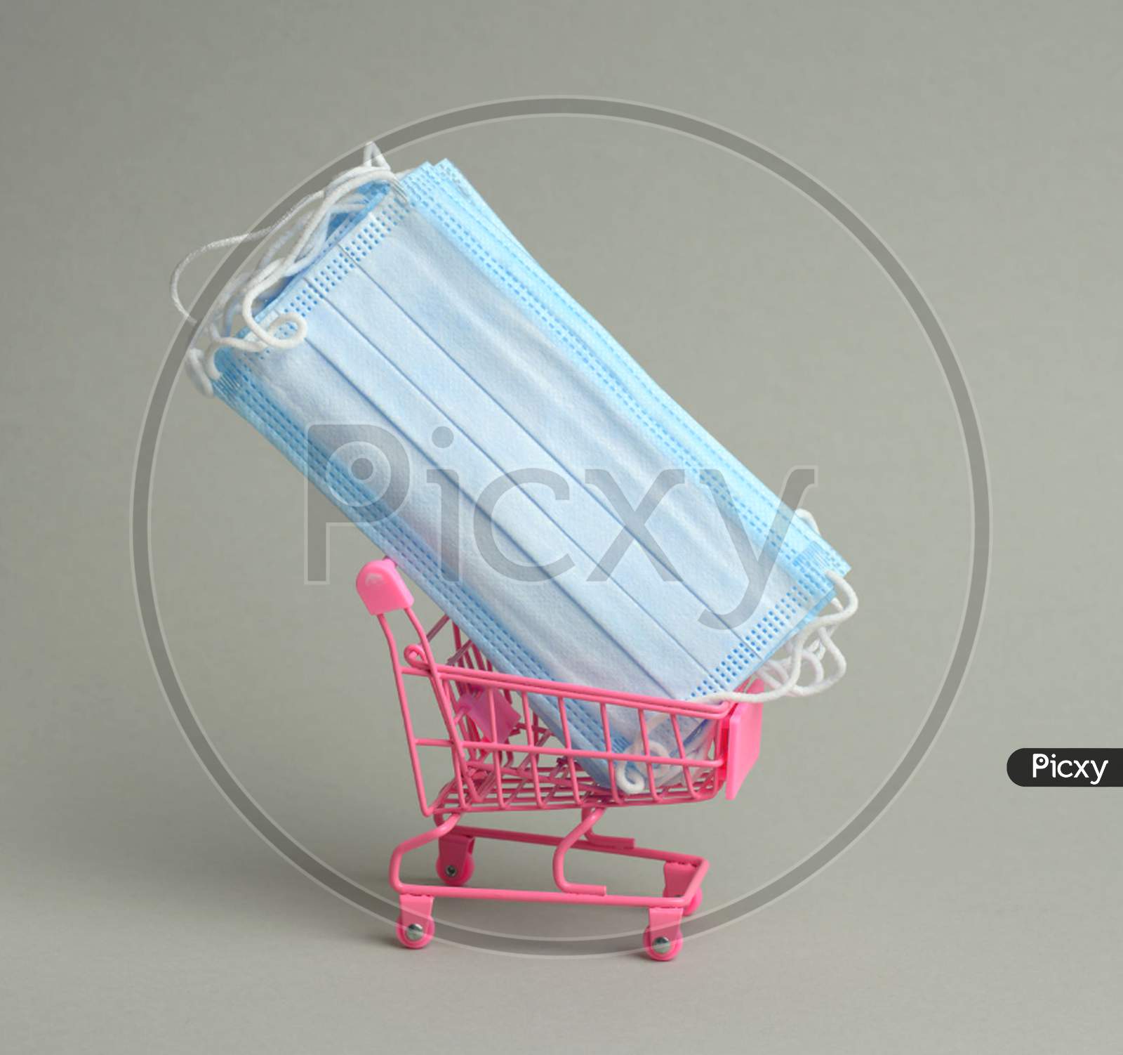 Stack Of Blue Disposable Medical Masks In A Pink Miniature Trolley On A Gray Background. Sale Of Medical Devices Online