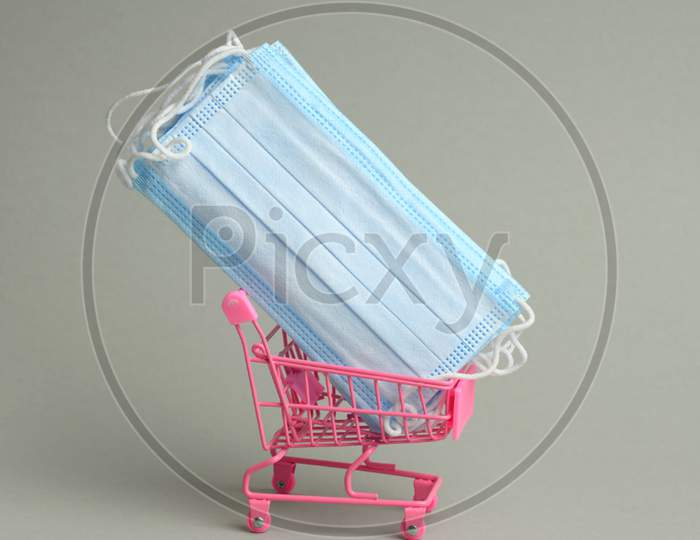 Stack Of Blue Disposable Medical Masks In A Pink Miniature Trolley On A Gray Background. Sale Of Medical Devices Online
