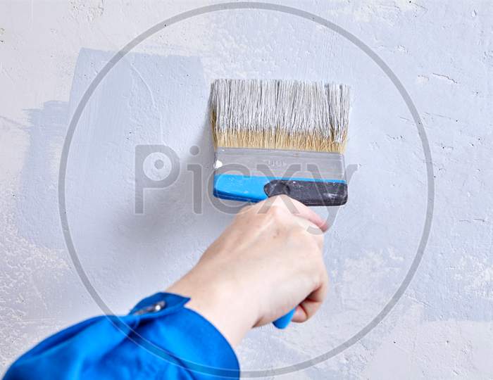 Painter Paints The Wall With A Paintbrush. Handyman Is Covering Beton With Color Using Paint Brush During Renovation.