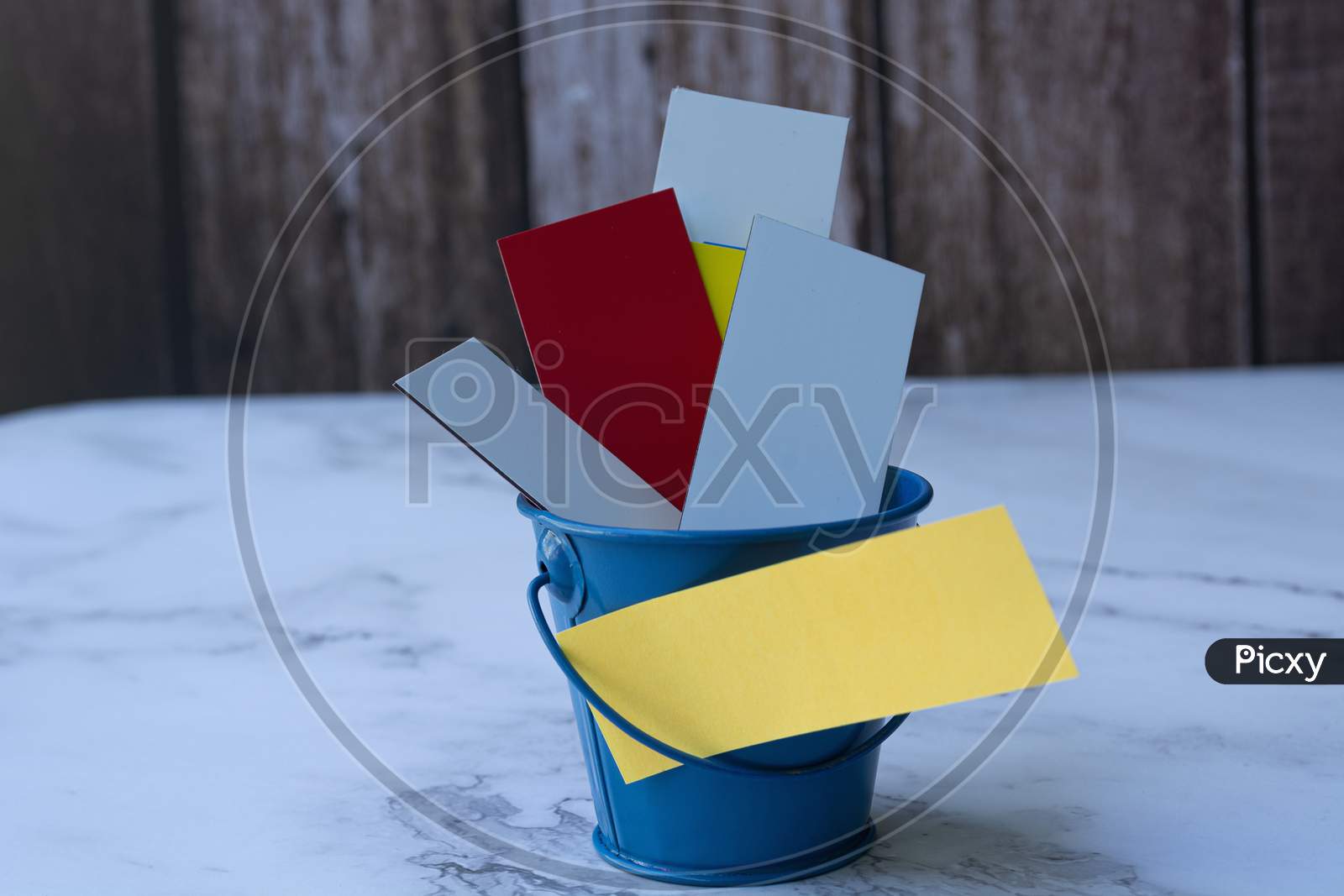 Colorful Papers Inside Of A Blue Bucket. Space For Text