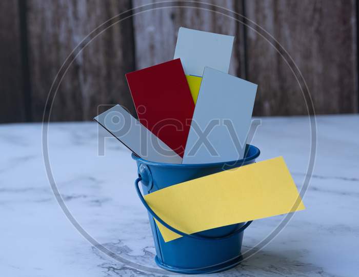 Colorful Papers Inside Of A Blue Bucket. Space For Text