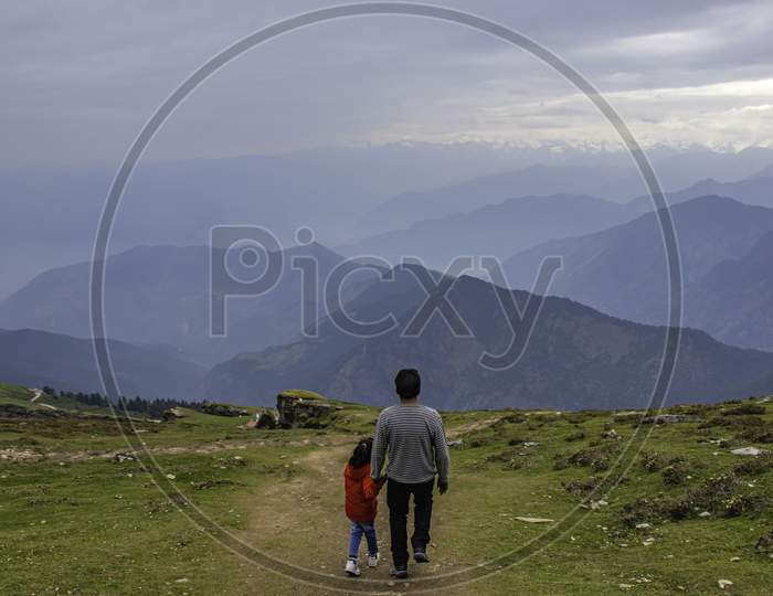 Father Holding The Hand Of Her Girl Child Taking Her Down From The Hills With Beautiful Himalayan Range In Front.