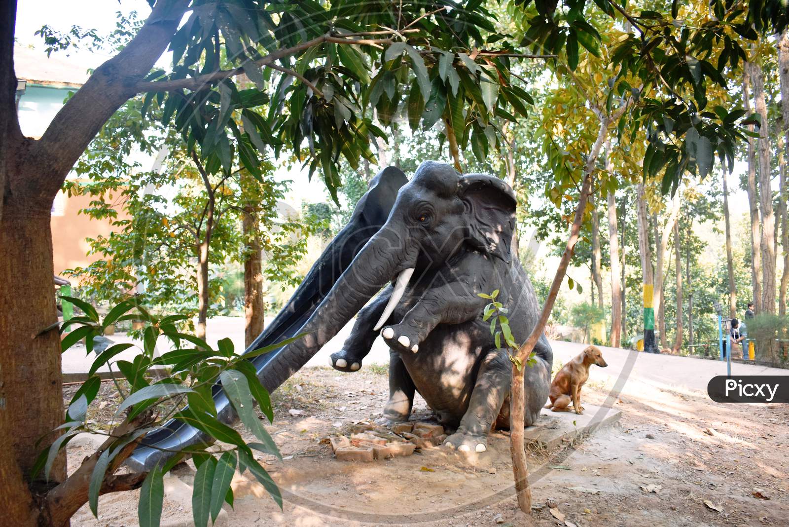 A Dog Sitting Beside A Artificial Elephant In A Playground