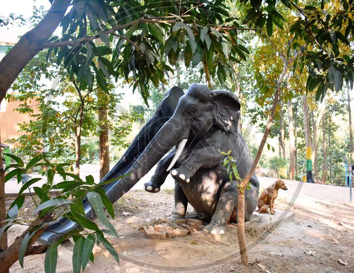 A Dog Sitting Beside A Artificial Elephant In A Playground