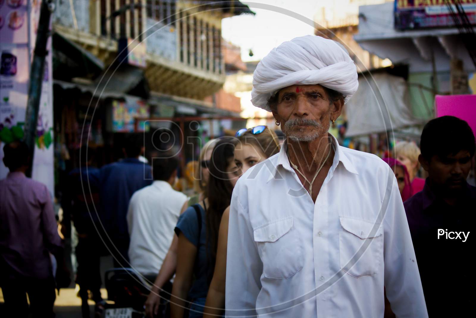 Pushkar, India - November 10, 2016: An Old Rajasthani Man In Traditional Ethnic Wear Such As White Turban And Typical White Kurta Walking In A Street During Pushkar Fair In The State Of Rajasthan