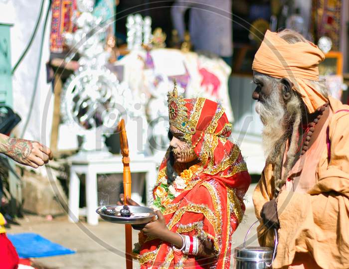 Pushkar, India - November 10, 2016: A Young Little Girl Dressed Up Or Disguised As Indian Goddess With Crown, Red Dress And Trishul To Attract Tourist Getting Money As Street Performer In Famous Fair