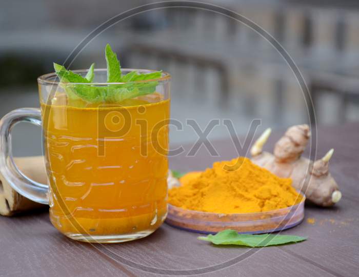Closeup The Brown Yellow Color Turmeric With Juice And Mint Over Out Of Focus Brown Background.