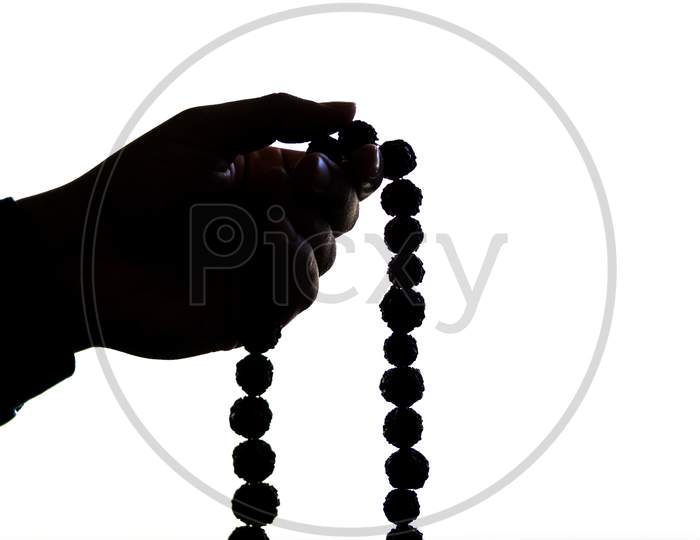 Silhouette Image Of Prayer Beads In Hand. Male Hand Holding Rosary, Praying To God On White Background, Religious Spirituality. Man Holding Rosary Beads And Meditating. Religious Concept