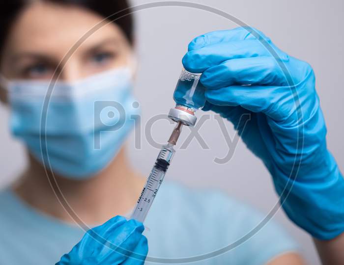 Doctor Scientis In Protective Gloves And Mask Holding Glass Vial With Injection Liquid. Vaccination Against Influenza And Coronavirus.