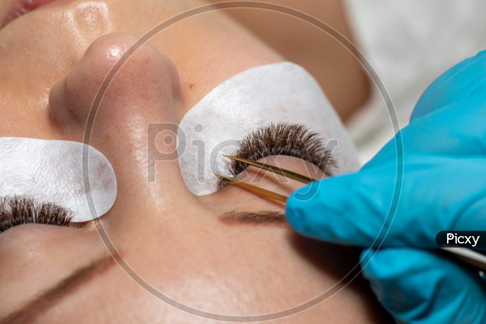 Treatment Of Eyelash Extension With Tweezers. Woman Eyes With Long Extended Lashes