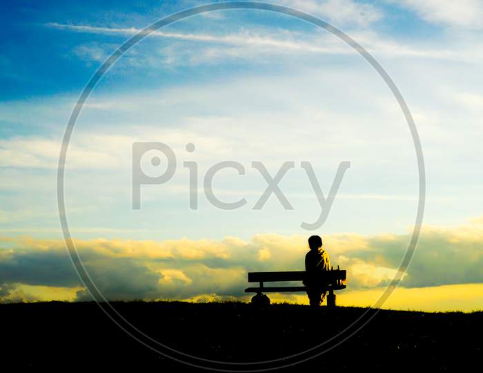 Silhouette Of A Woman Sitting On A Sunset Hill