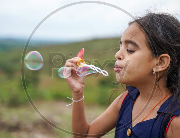 Young Girl Kid Playing By Blowing Soap Water Bubbles - Conept Of Playful Chidlren During Holiday Vacation.