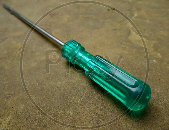 Screwdriver In Green Handle Hardware Tool Presented On Stone Floor For Industrial Background.