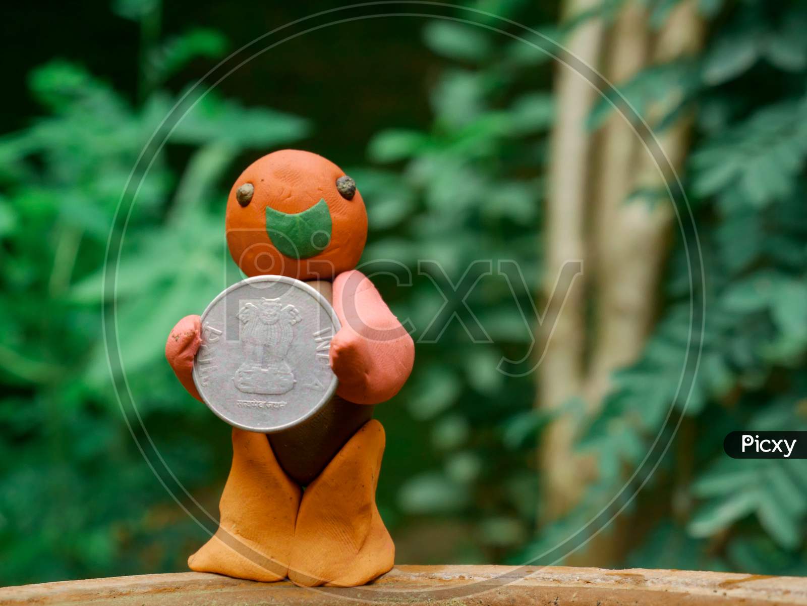 Image of Indian Government Currency Coin Presented By Clay Soft Toy Man  Around Green Blur Leaves Background.-JY491056-Picxy