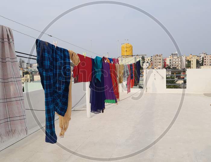Washed Wet Cloths Hanged In A Terrace With Thread And Plastic Clips At The Building Top