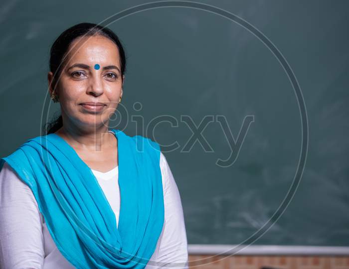 Portrait of a Smiling   Woman teacher in front of Blackboard in Class room