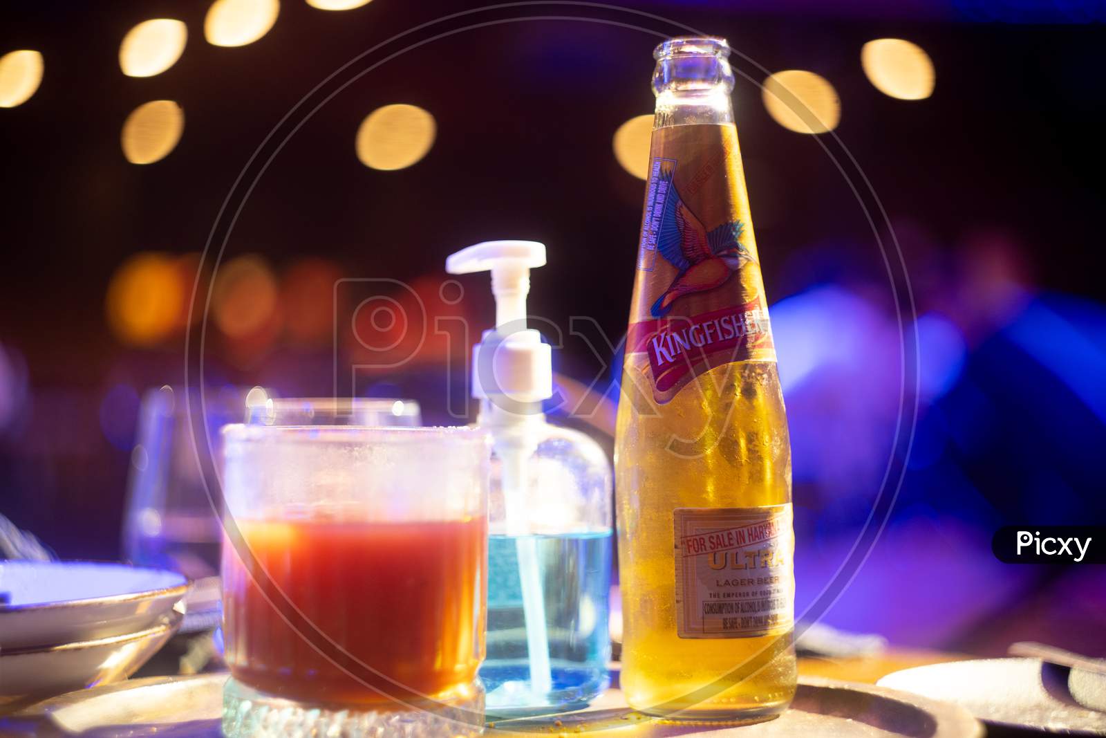 Image Of Famous Indian Beer Brand Kingfisher Bottle With Bubble Coming Out With Out Of Focus Background Lights With Bokeh Balls Showing It Placed In A Bar Club Pub Nightlife Spot In