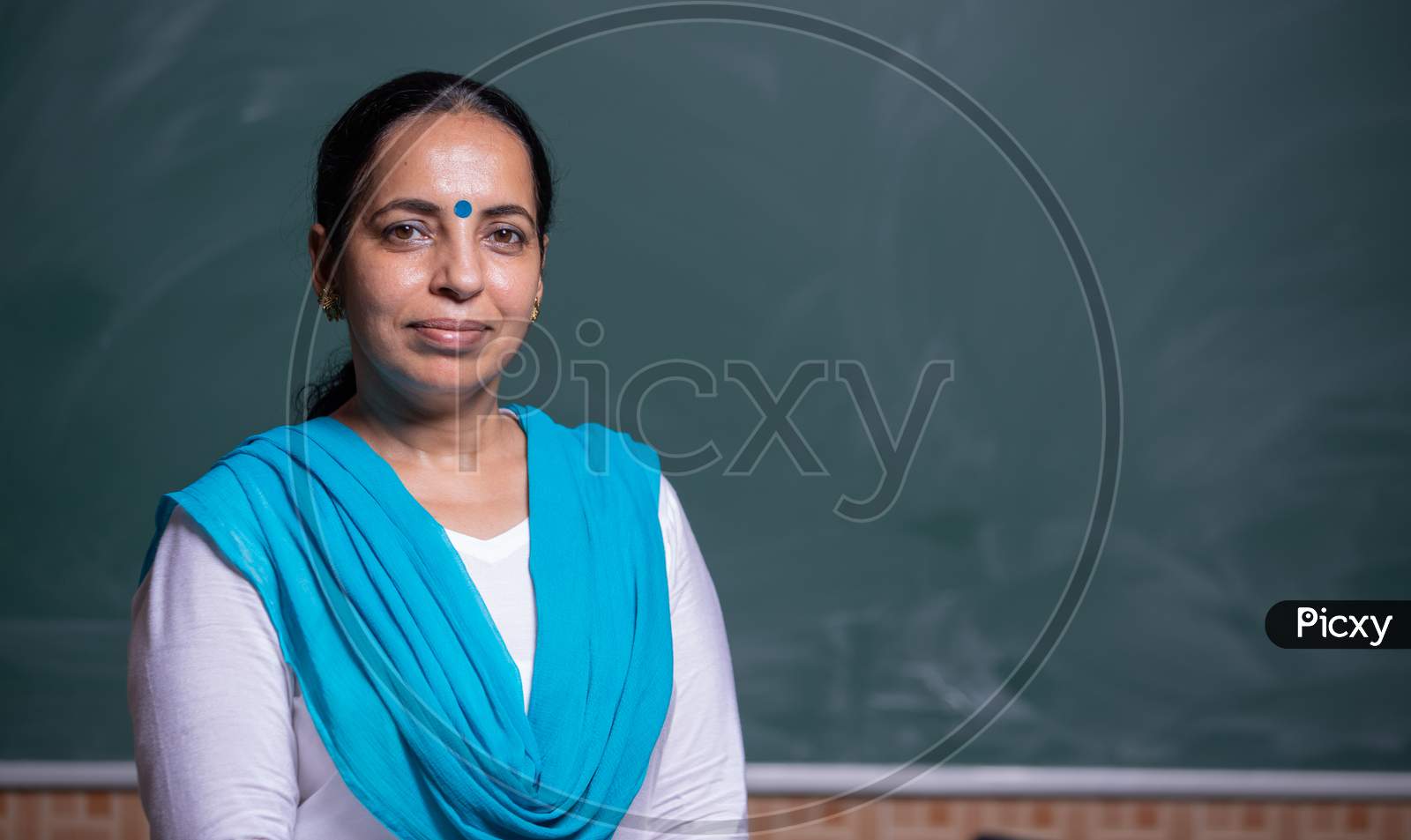 Portrait of a Smiling   Woman teacher in front of Blackboard in Class room