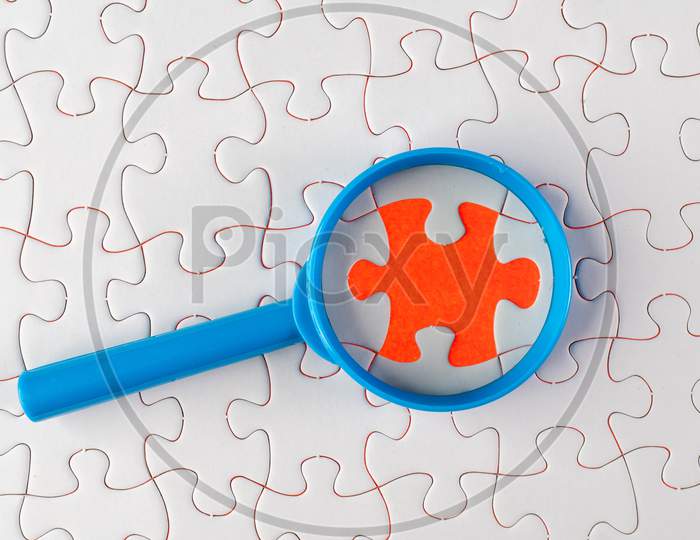 A Magnifying Glass On White Jigsaw Puzzle.