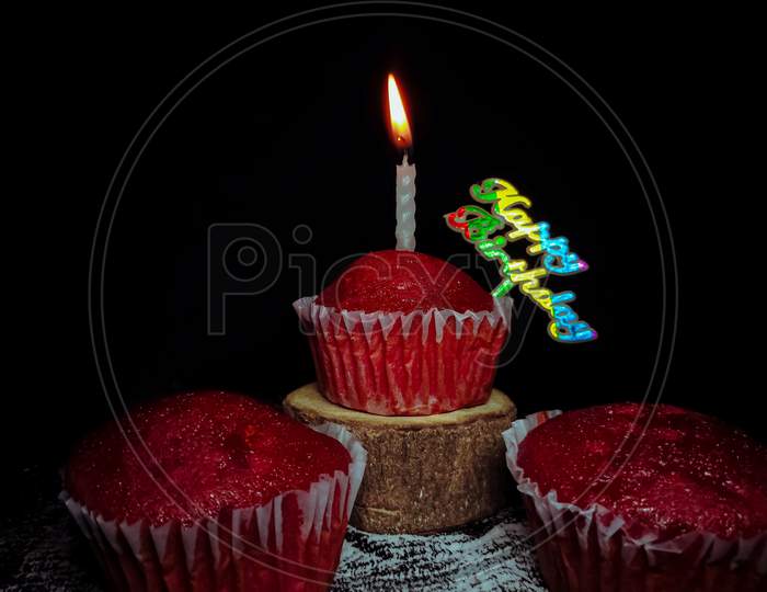 Closeup of Delicious Red Velvet cupcakes or muffins decorated with candle and Happy birthday sign on top.