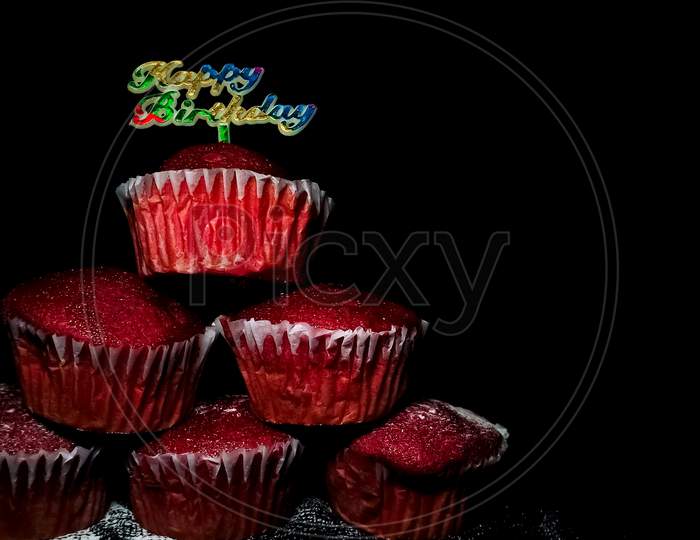 Closeup of Delicious Red Velvet cupcakes or muffins decorated with sprinkles and happy birthday sign on top.