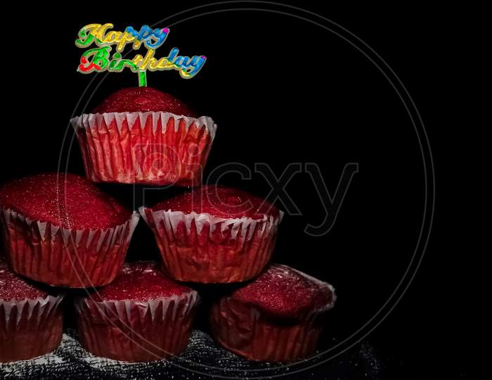 Closeup of Delicious Red Velvet cupcakes or muffins decorated with sprinkles and happy birthday sign on top.