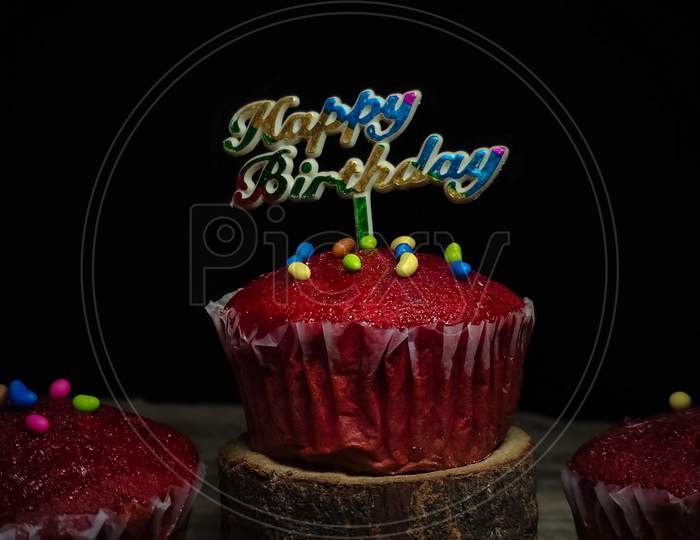 Closeup of Delicious Red Velvet Birthday cupcakes or muffins decorated with sprinkles and Happy birthday sign on  on top.