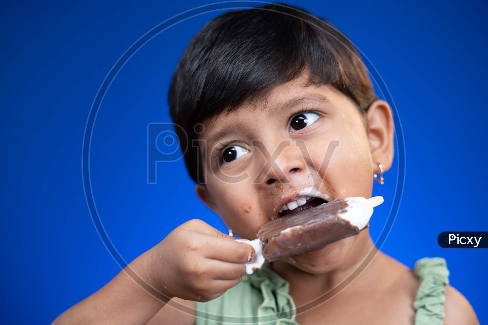 Cloe Up Head Shot Of Girl Kid Busy Eating Ice Cream On Blue Studio Background - Concept Of Unhealthy Food Consumption