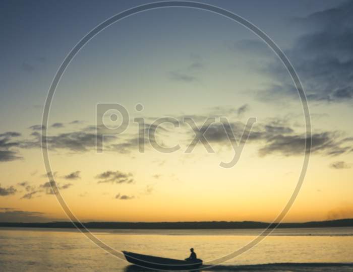 Small Fisherman Barge Sailing In The Lagoon During Sunset. Backlighting Of A Human Figure