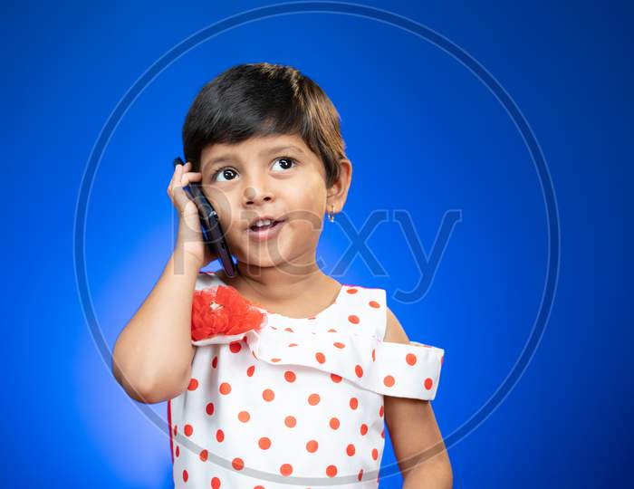 Happy Cute Girl Kid Busy Talking On Mobile Phone In Studio Blue Background
