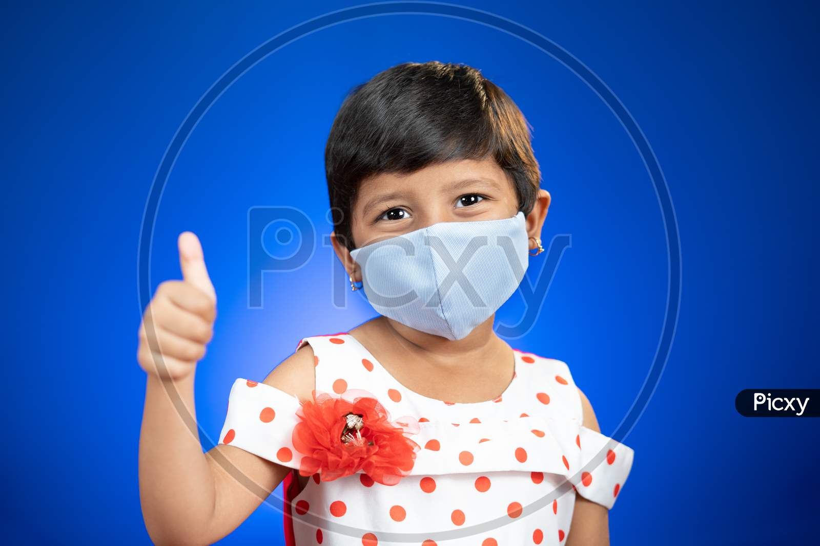 Little Girl Kid Adjusting Medical Face Mask And Showing Thumps Up Gesture - Concept Showing Of Coronavirus Covid-19 Saferty Measures By Wearing Mask As New Normal