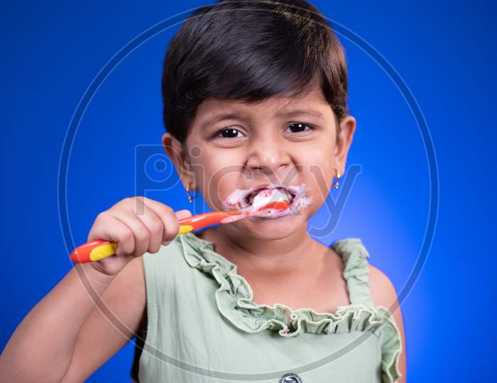 Portrait Of Girl Kid Brushing Teeth On Blue Color Background - Concept Of Child Healthy Tooth By Cleaning Daily