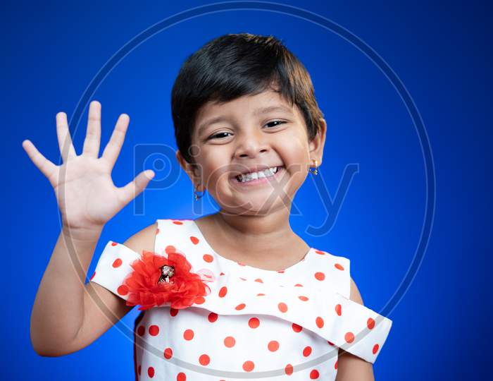 Cute Little Girl Kid Saying Hi Anf How Are How By Looking At Camera On Blue Color Background - Concept Of Child Greeting.