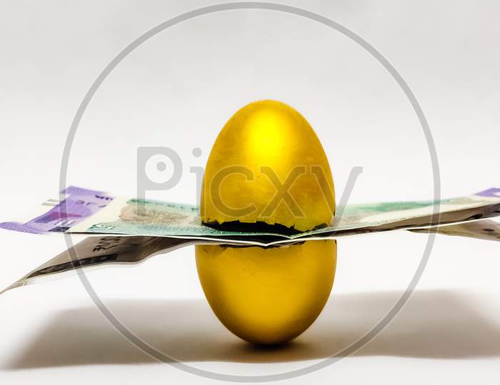 Closeup of Broken Golden egg with indian coins and bills inside isolated in a White background with selective focus on egg symbolizing the concept of retirement money. Savings.