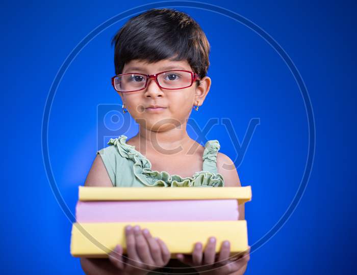 Young Smiling Lttile Girl Kid Holding Bunch Of Books With Eye Glasses On Blue Background - Concep Of Child Book Nerd, Prodigy And Back To School