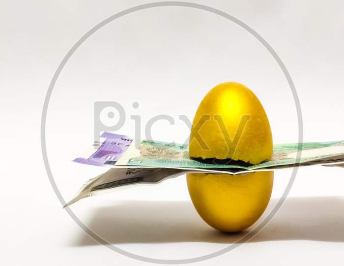 Closeup of Broken Golden egg with indian coins and bills inside isolated in a White background with selective focus on egg symbolizing the concept of retirement money. Savings.