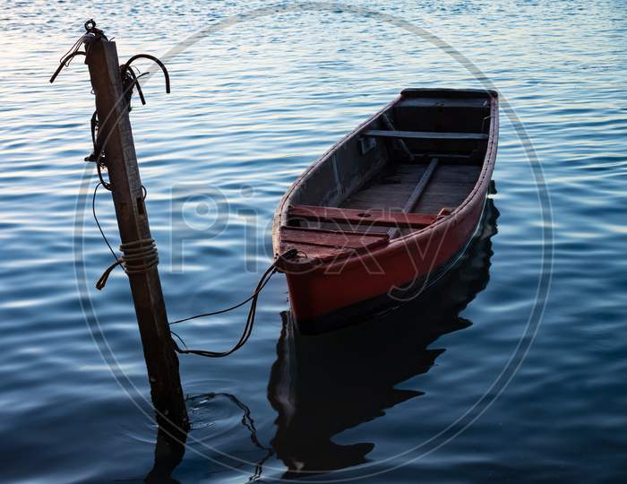 Small Fisherman Boat Moored On The Shore Of The Lake With Calm Waters.