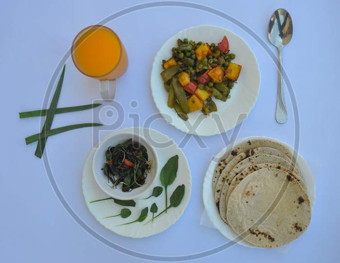 Overhead view of matar paneer mix veg, saag (greens), roti (chapati) and juice on glass isolated over white background