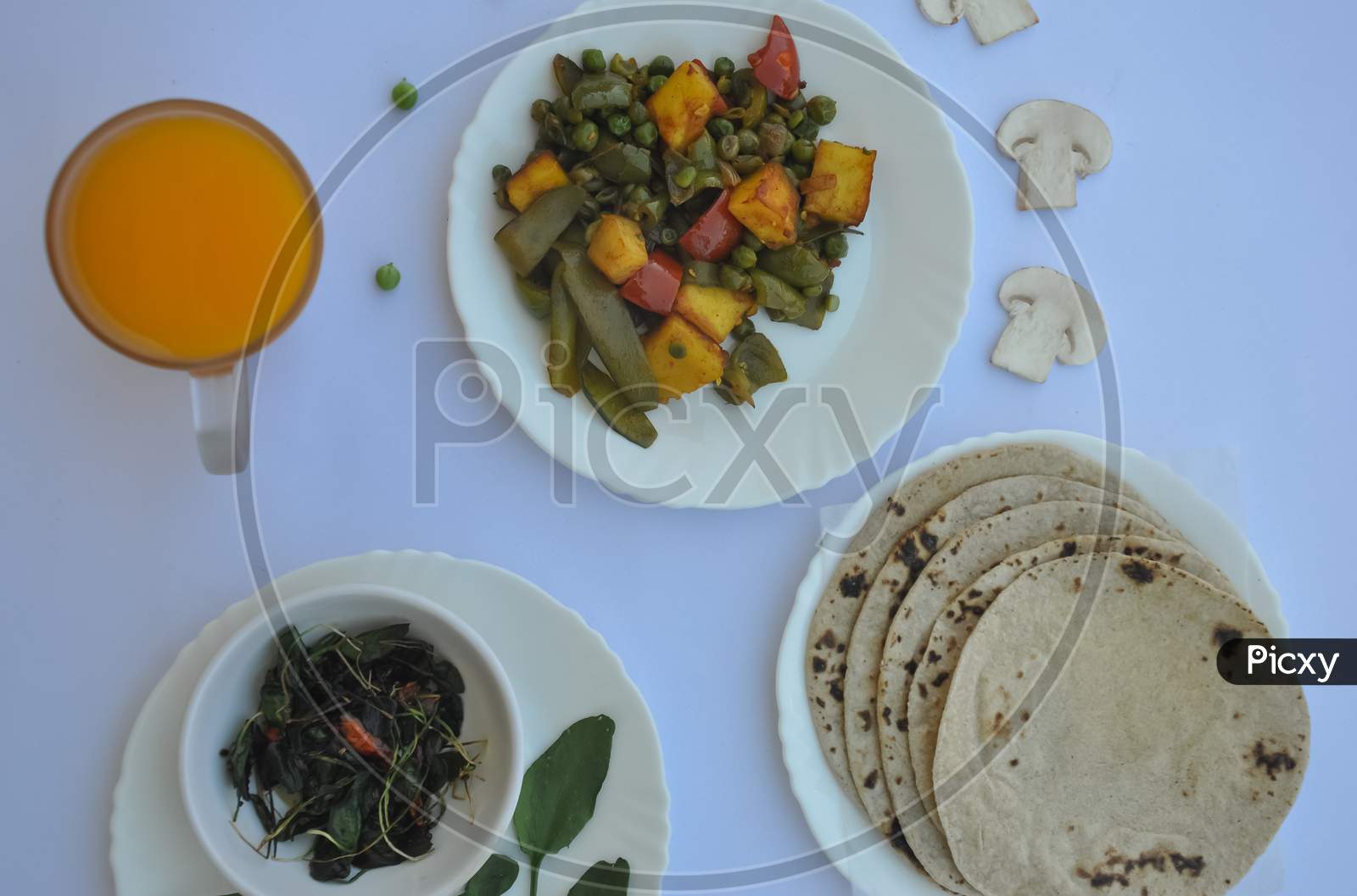 Overhead view of matar paneer mix veg, saag (greens), roti (chapati) and juice on glass isolated over white background