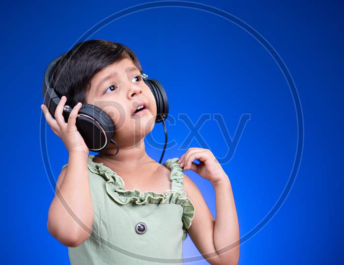 Happy Liitle Kid With Headphones Enjoying Favourite Song By Singing Loudly On Blue Background.