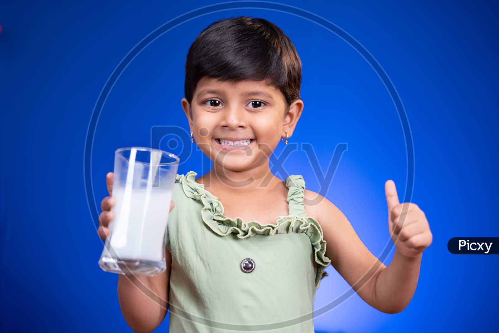 Little Girl Kid With Milk In Hand Showing Thumbs Up Sign On Blue Background - Concept Showing To Encouragement Or Recommending Milk For Children's Health