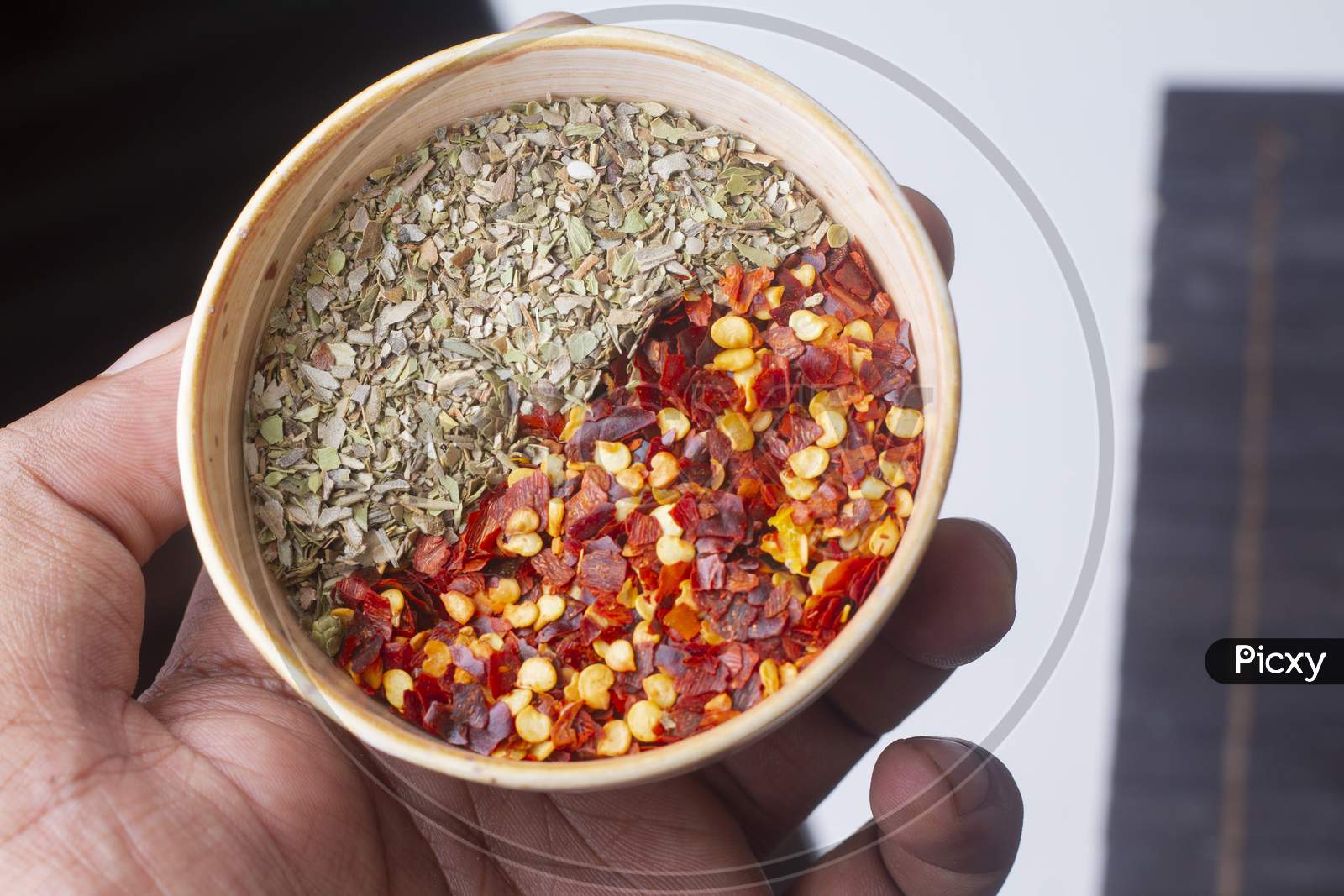 Chili Flakes And Oregano Bowl In Hand Isolated On Light Background