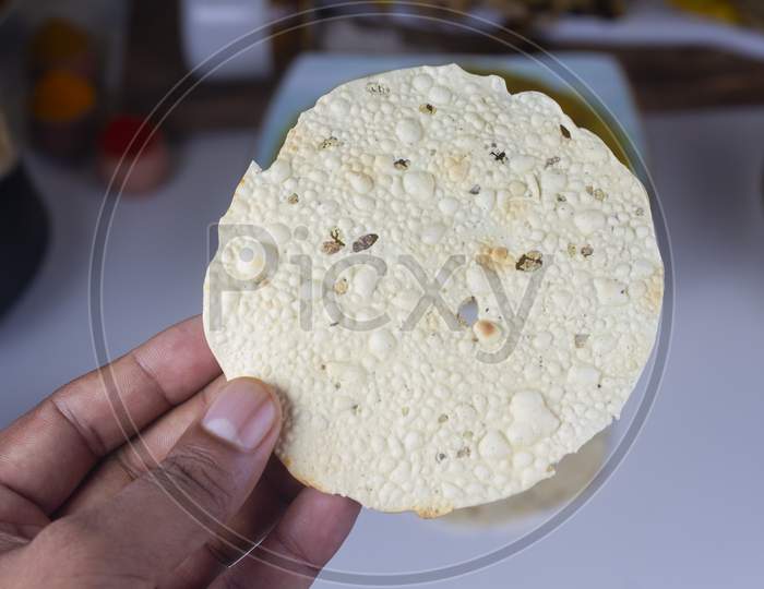 A Person Holding Indian Snack Papd In Hand Isolated On Light Background.