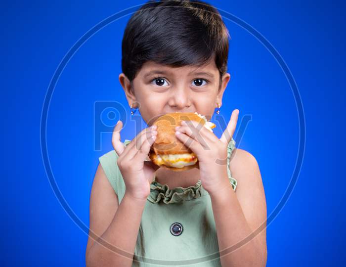Girl Kid Enjoying Eating Of Tasty Burger On Blue Background - Concept Of Children Unhealthy Eating Habits.