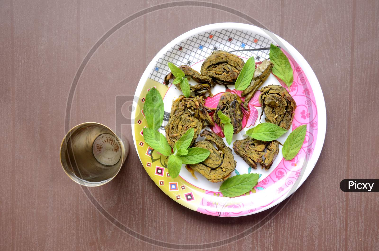 Closeup The Fried Arabic Leaves Food With Green Mint In The Plate And Water Brass Glass Over Out Of Focus Brown Background.