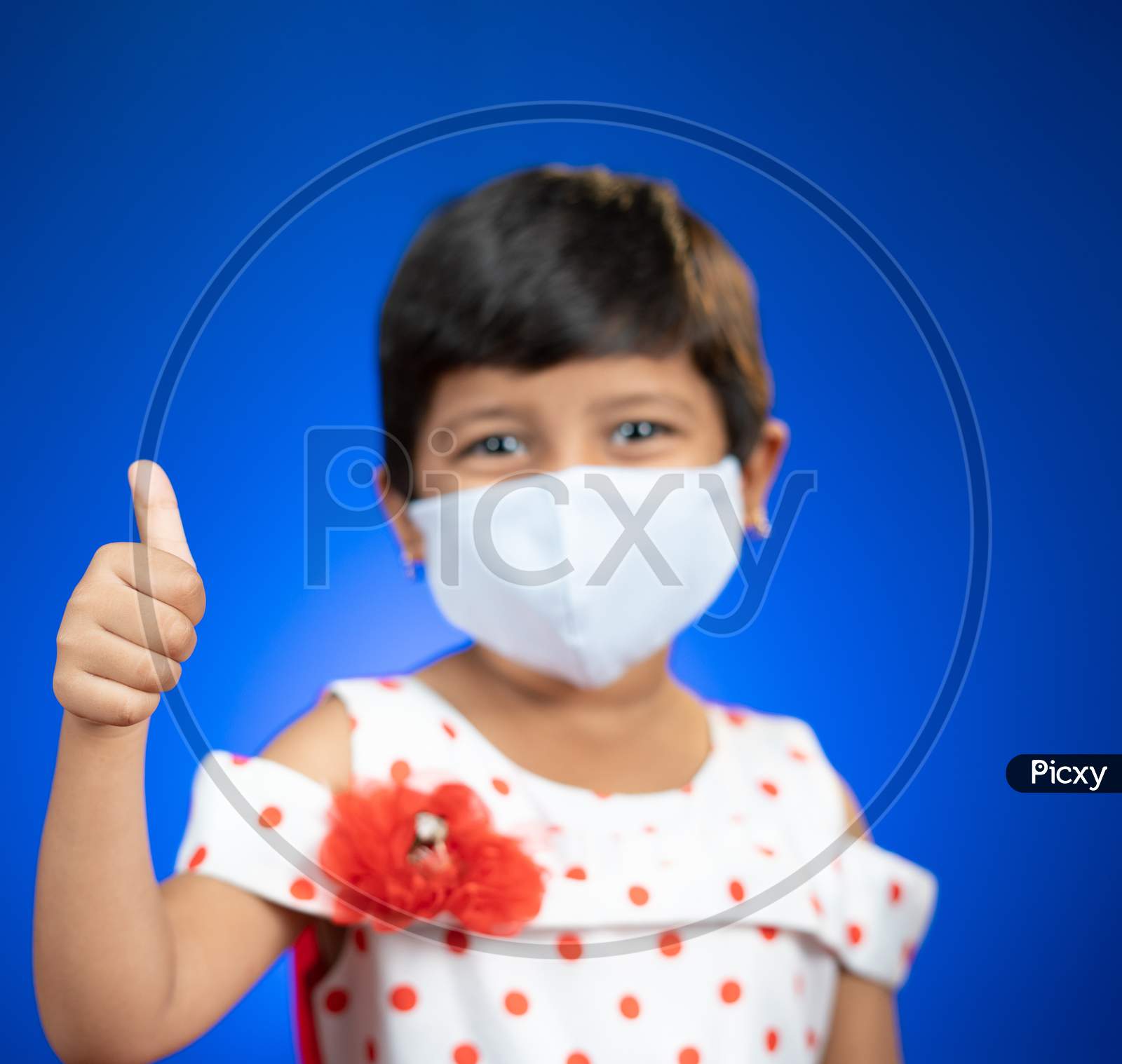 Focus On Thumb, Little Girl Child With Medical Face Mask Showing Thumps Up Gesture - Concept Showing Of Coronavirus Covid-19 Saferty Measures By Wearing Mask.