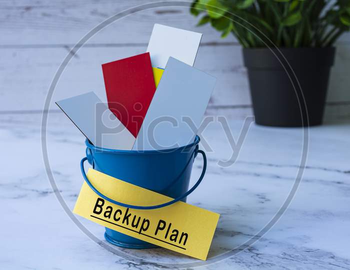 Text On Yellow Paper With Colorful Paper Inside Of A Blue Bucket. Backup Plan
